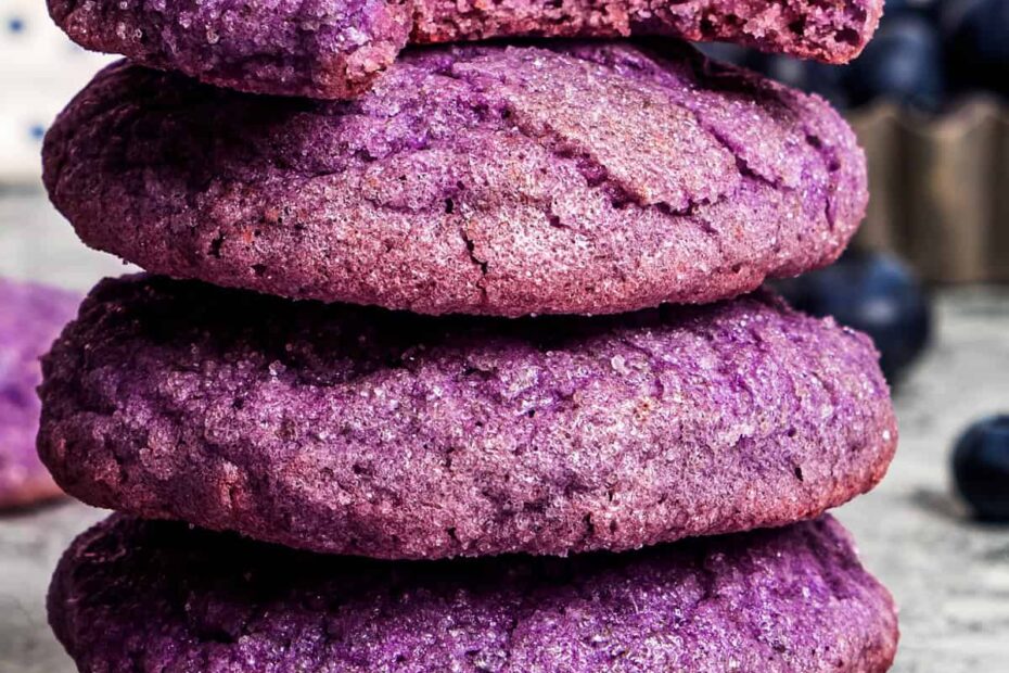 A stack of blueberry cookies on a countertop with a bite missing from the top cookie.