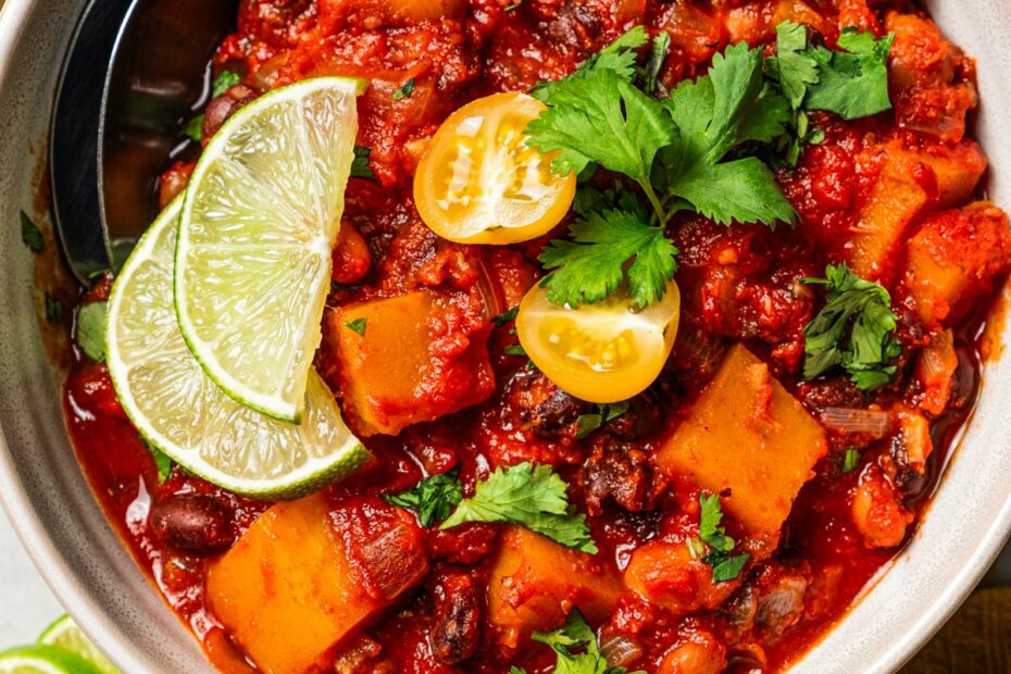 A bowl of butternut squash chili garnished with lime wedges.