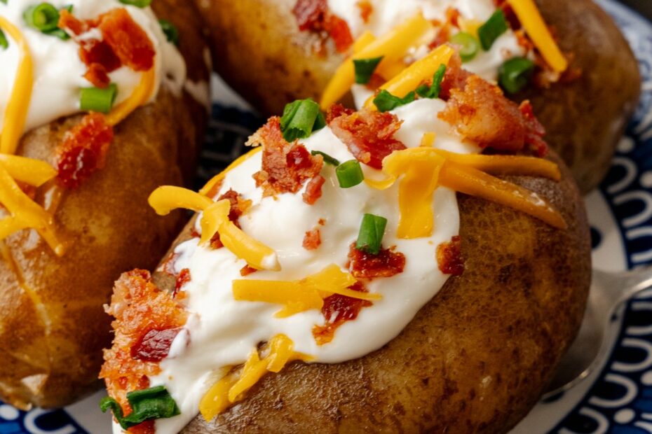 Baked potatoes topped with sour cream cheese bacon bits and chives ontop of a nice blue plate.