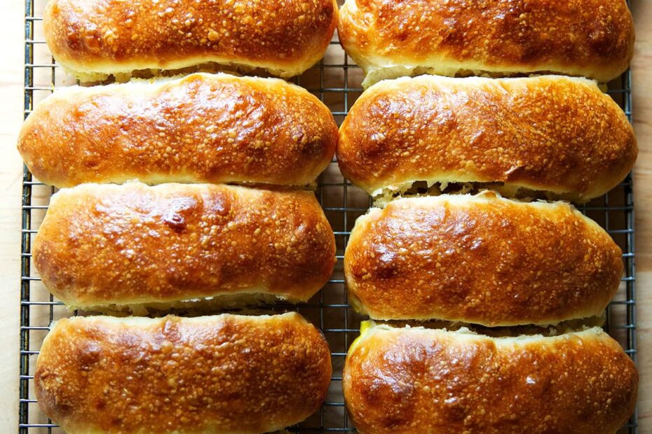 Twelve just-baked brioche hot dog buns on a cooling rack.