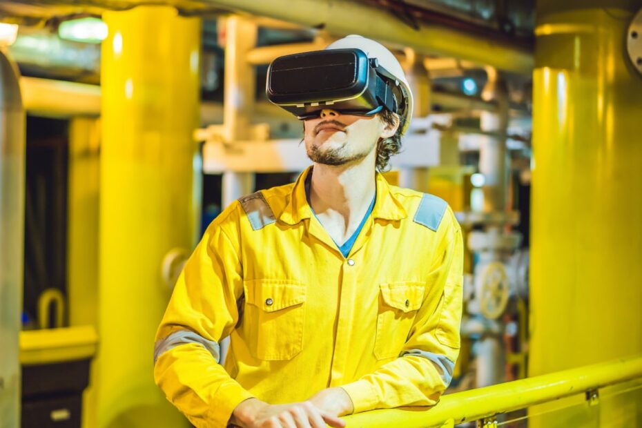 A man wears a VR headset and bright yellow overalls in an industrial setting.