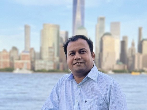 Sajal Rastogi from Kyvos Insights wears a pale shirt and stands by a water in front of the New York skyline.