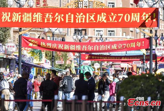 Tourists walk under banners celebrating the 70th anniversary of the Xinjiang Uygur Autonomous Region at the International Grand Bazaar pedestrian street in Urumqi, Xinjiang on Sept. 22, 2025. (Photo: China News Service/Liu Xin)