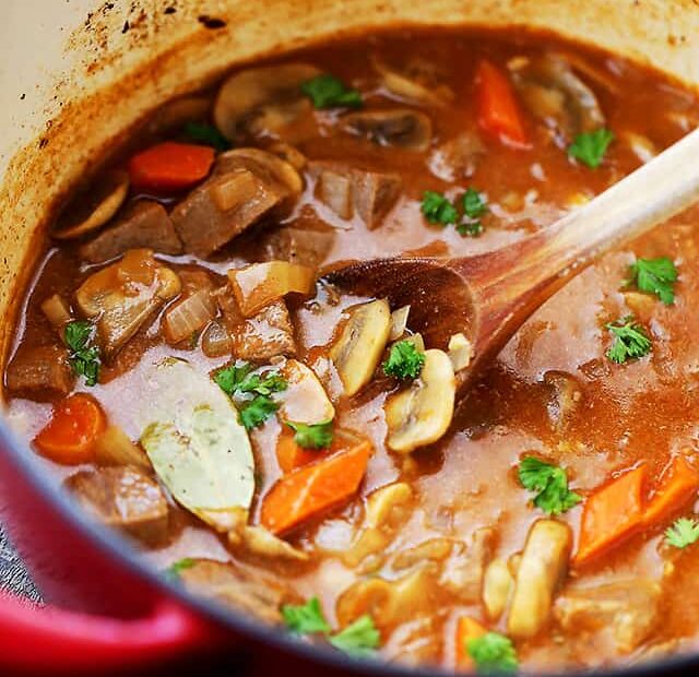 Beer beef stew in a red Dutch oven with a wooden spoon.
