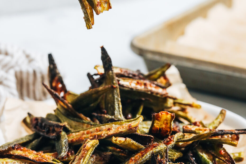 Fork holding up a few slices of crispy oven roasted okra over a plate of more baked okra