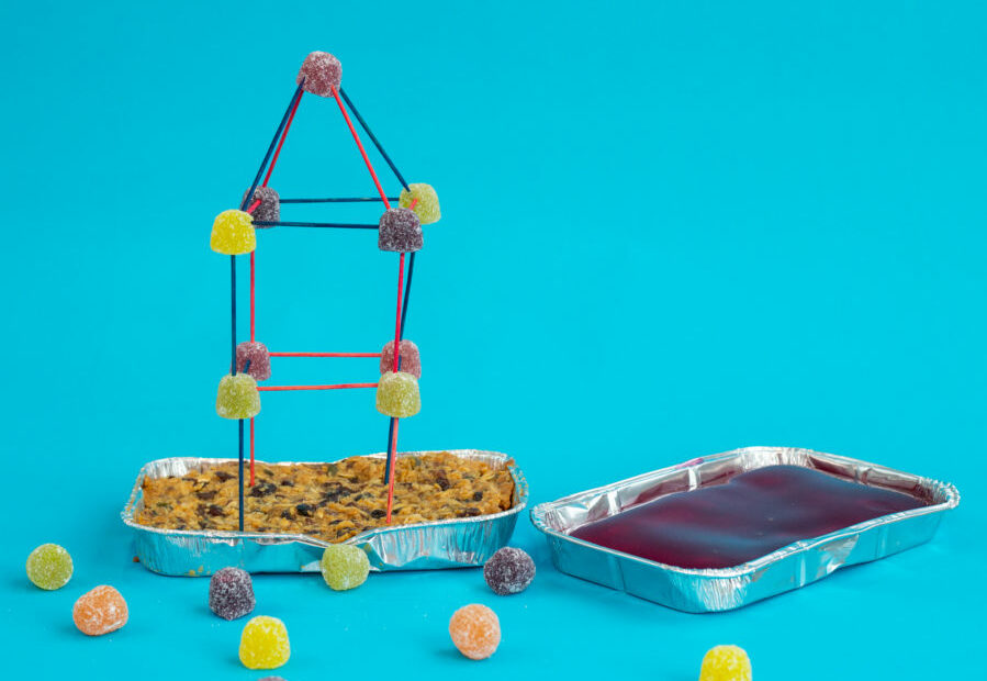Two foil trays one filled with jelly/jello and one flapjack. The flapjack tray has a tower made from toothpicks and gummy sweets in the flapjack base. For an earthquake science experiment .