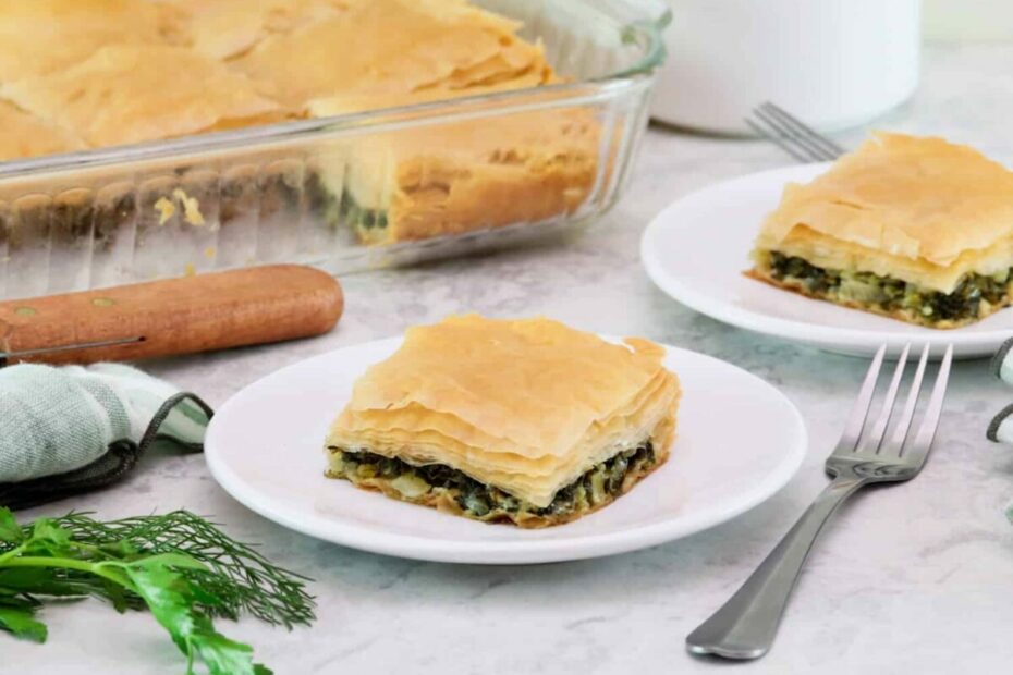 Two white plates containing square slices of vegan spanakopita.