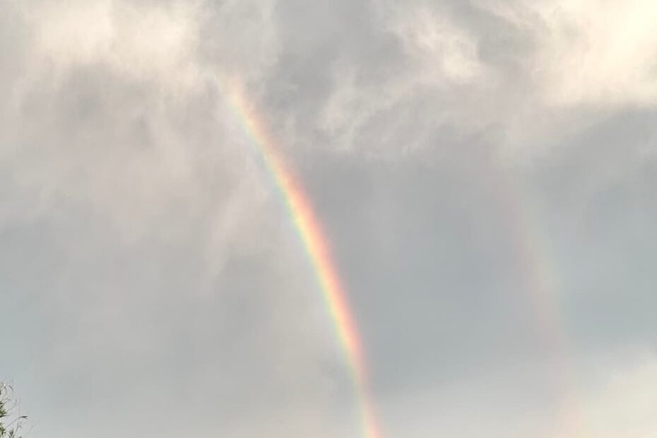 dark storm clouds in the sky with a colorful double rainbow cutting through down to a house