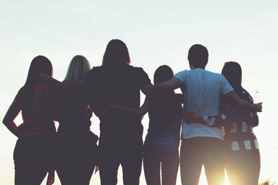 Group of people standing together with arms around each other at sunset, symbolizing unity and community.