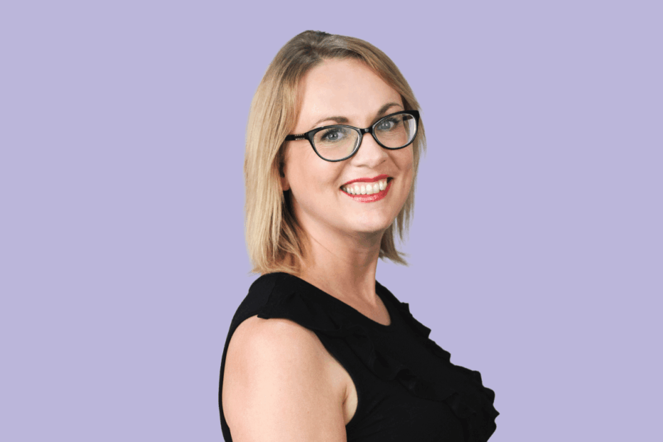 Lorna Ferrie has blonde hair and glasses and poses in front of a plain purple background.