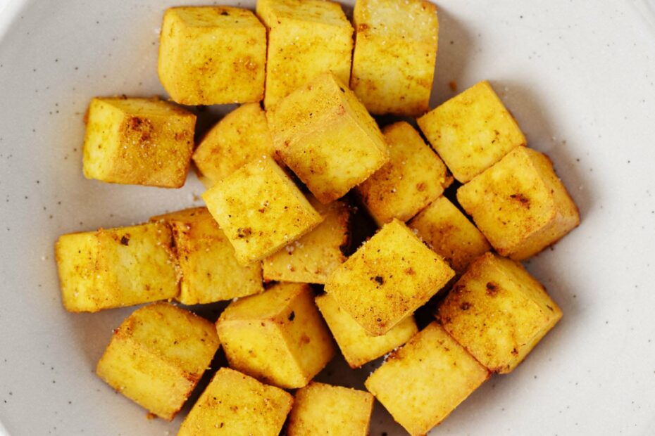 A round, wide-rimmed white bowl holds bright golden baked curried tofu cubes.