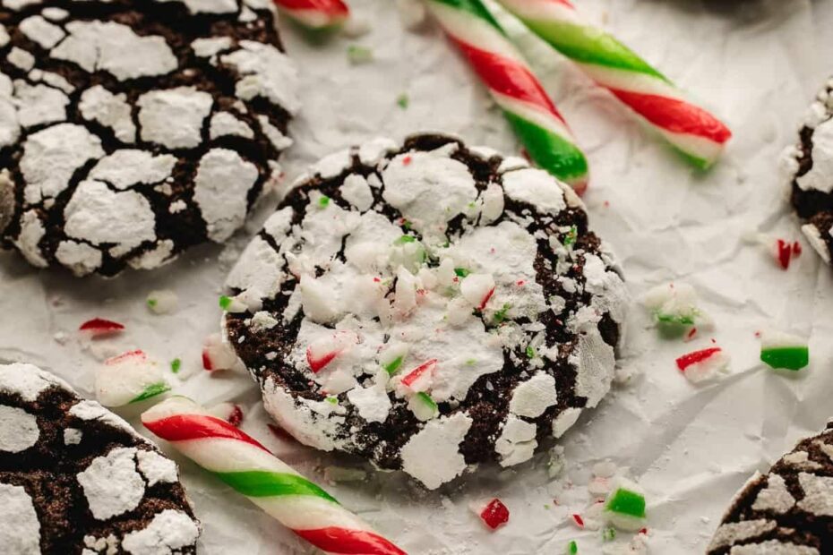 Crinkle chocolate peppermint cookies with candy canes and festive sprinkles on parchment paper.