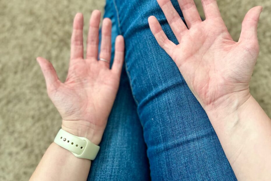 Person sitting on the ground with their legs outstretched with their open hands out, palms showing