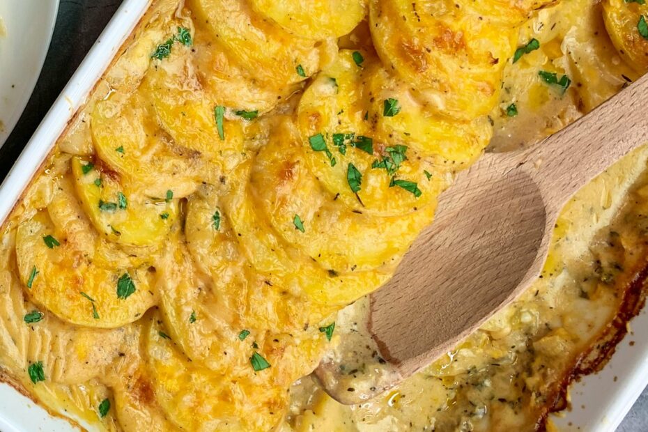 Baked scalloped potatoes in a white baking dish with a wooden spoon.