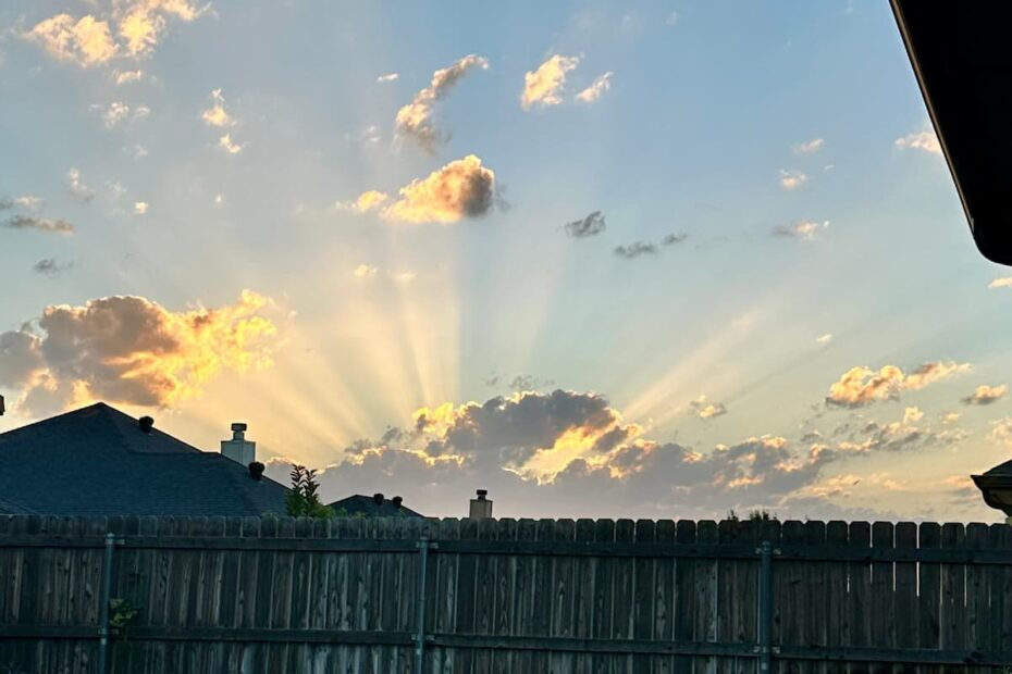 Stunning backyard sunrise with sun rays breaking through the clouds against a blue sky
