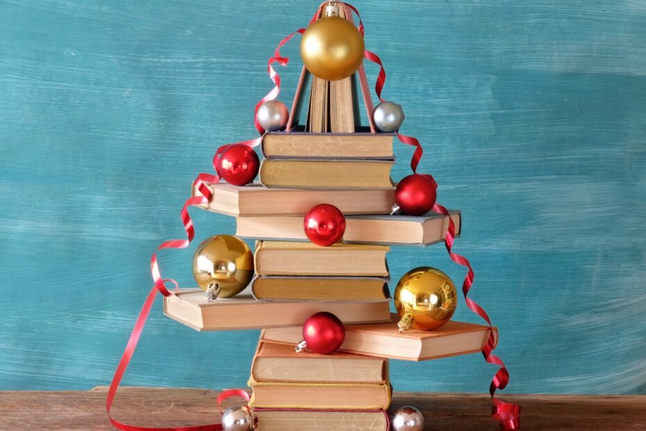 A pile of books arranged in the shape of a Christmas tree, with baubles and tinsel spread around it.