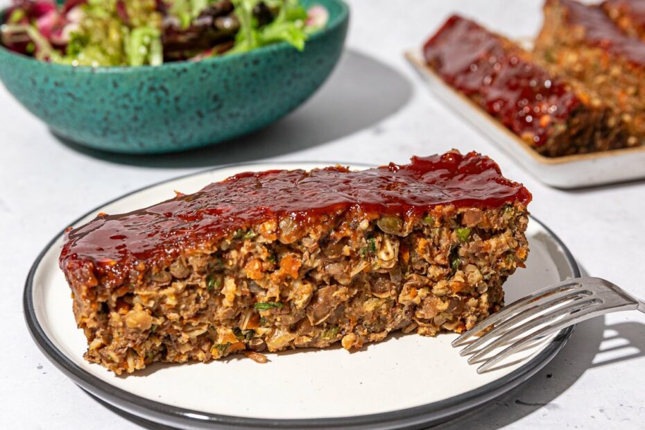 slice of lentil walnut loaf on white plate with blue bowl of salad behind it