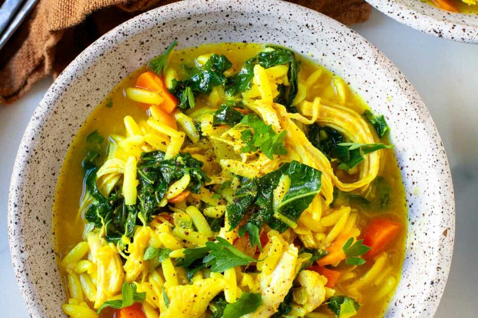 speckled grey bowl with chicken orzo soup with turmeric, kale, carrots and parsley on top
