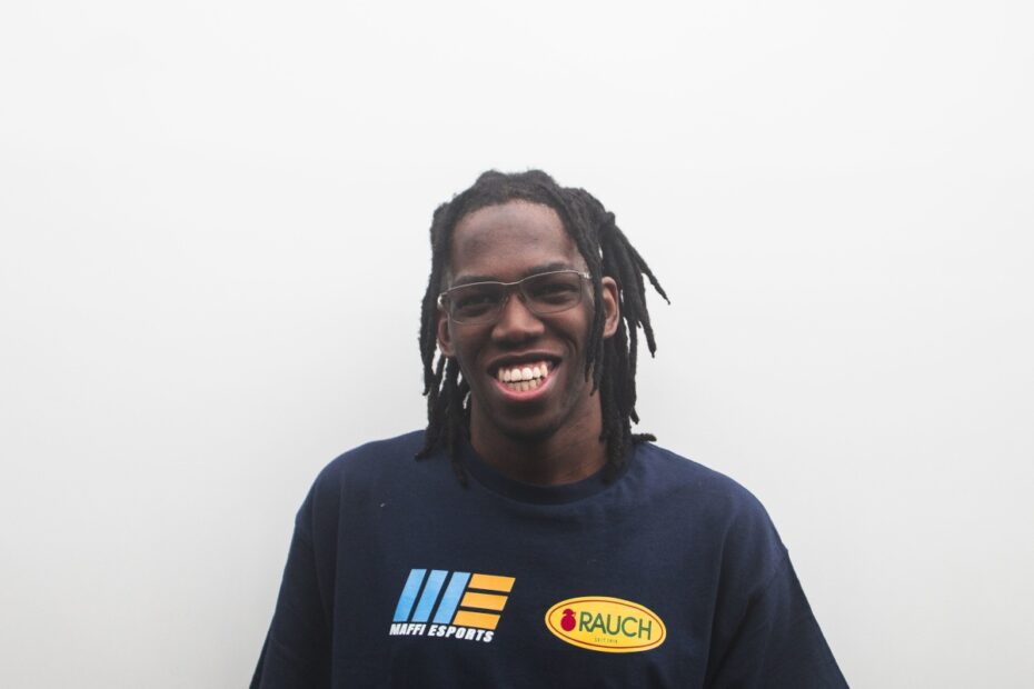 Kamto Chukwureh wears a racing t-shirt and smiles, standing against a white background.