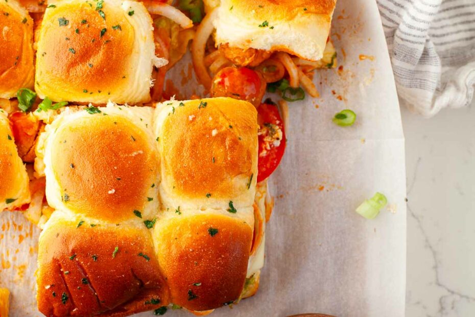 buffalo chicken meatball sliders with tomato and onion on parchment paper with blue cheese dressing in small bowl