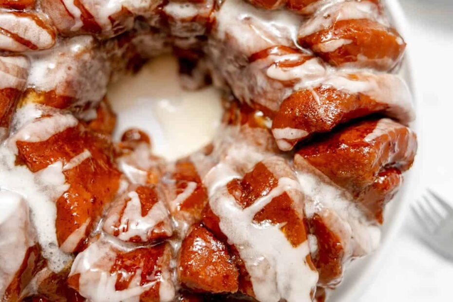 A close-up of a glazed monkey bread ring drizzled with white icing, served on a white plate.