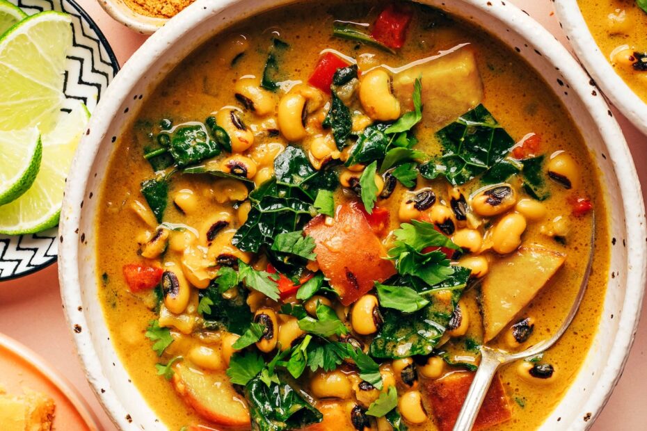 Overhead photo of a bowl of curried black eyed pea soup next to lime wedges, curry powder, and cornbread