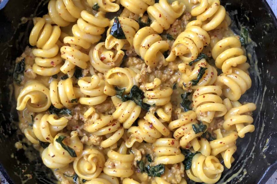 Creamy pumpkin pasta with sausage and kale in a cast iron skillet featuring trottole pasta coated in pumpkin cream sauce, an easy pumpkin pasta sauce recipe.