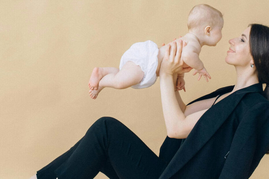 young stylish professional woman holds a baby; she has a blazer resting on her shoulders but is not wearing it